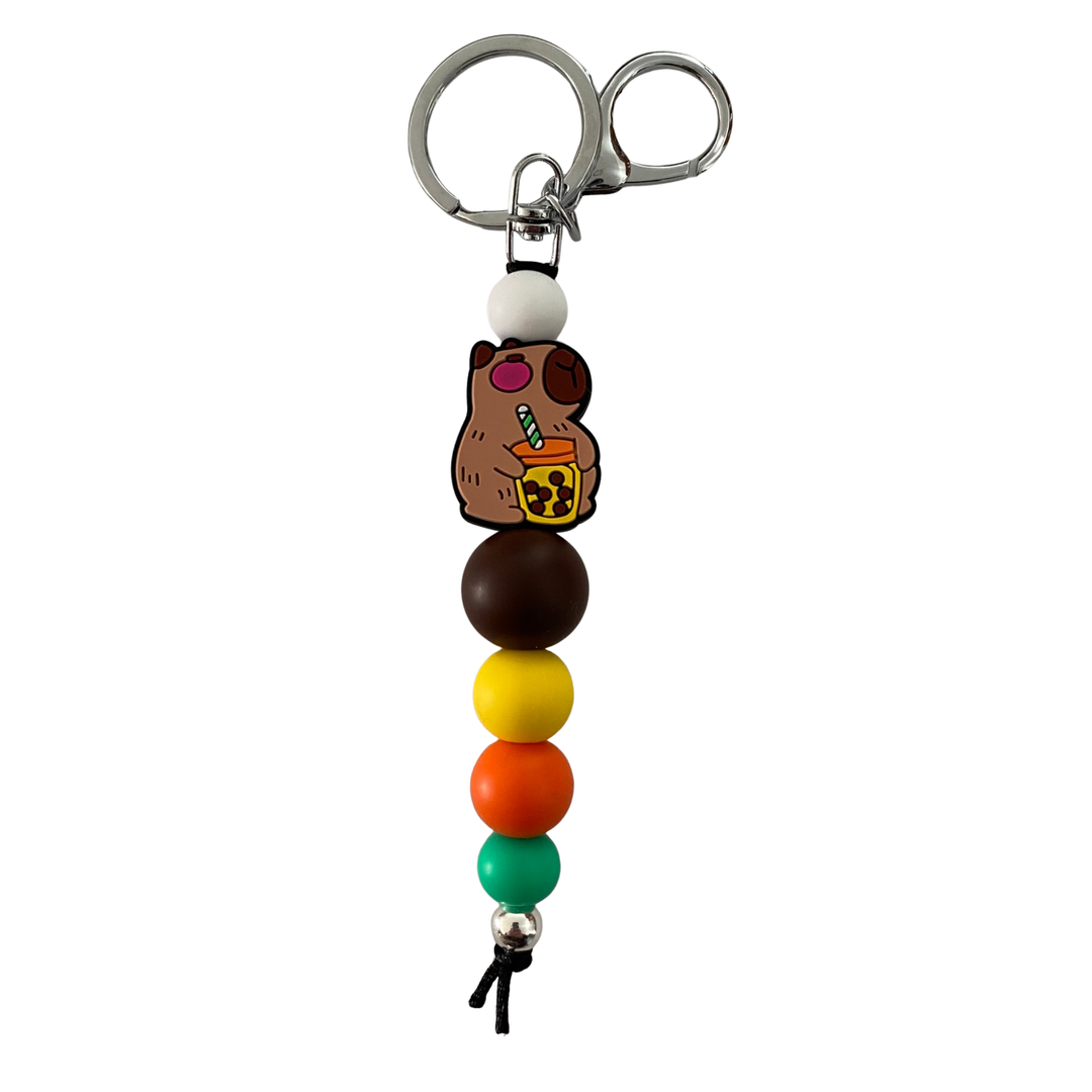 Capybara silicone keyring. Features white, brown, yellow, orange and green silicone beads, Capybara focal bead holding a tiny sippy cup and straw.