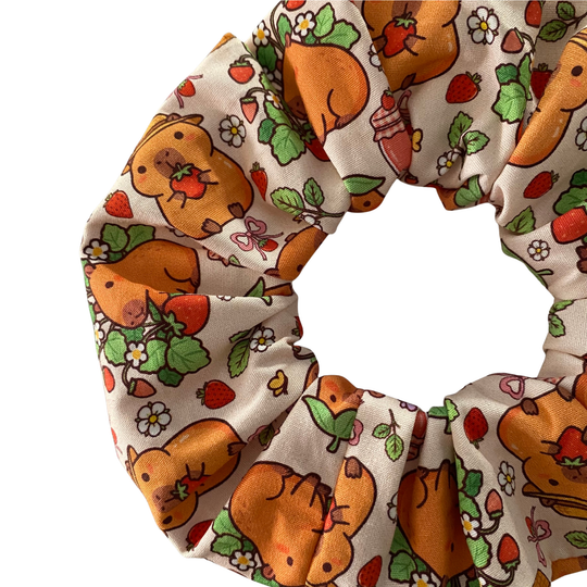 A close up view of a hair scrunchie featuring a cute cartoon capybara pattern on a apricot fabric.