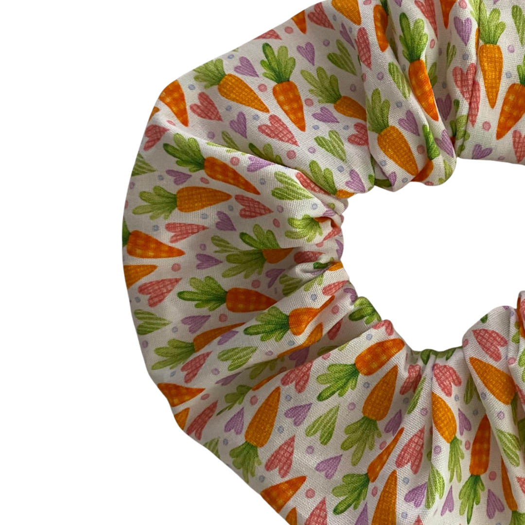 A close up view of a white fabric scrunchie featuring images of carrots and love hearts.