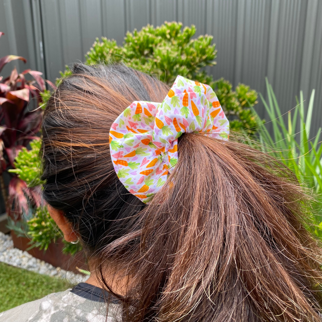 Person with a colourful carrot pattern scrunchie in their hair, surrounded by plants.
