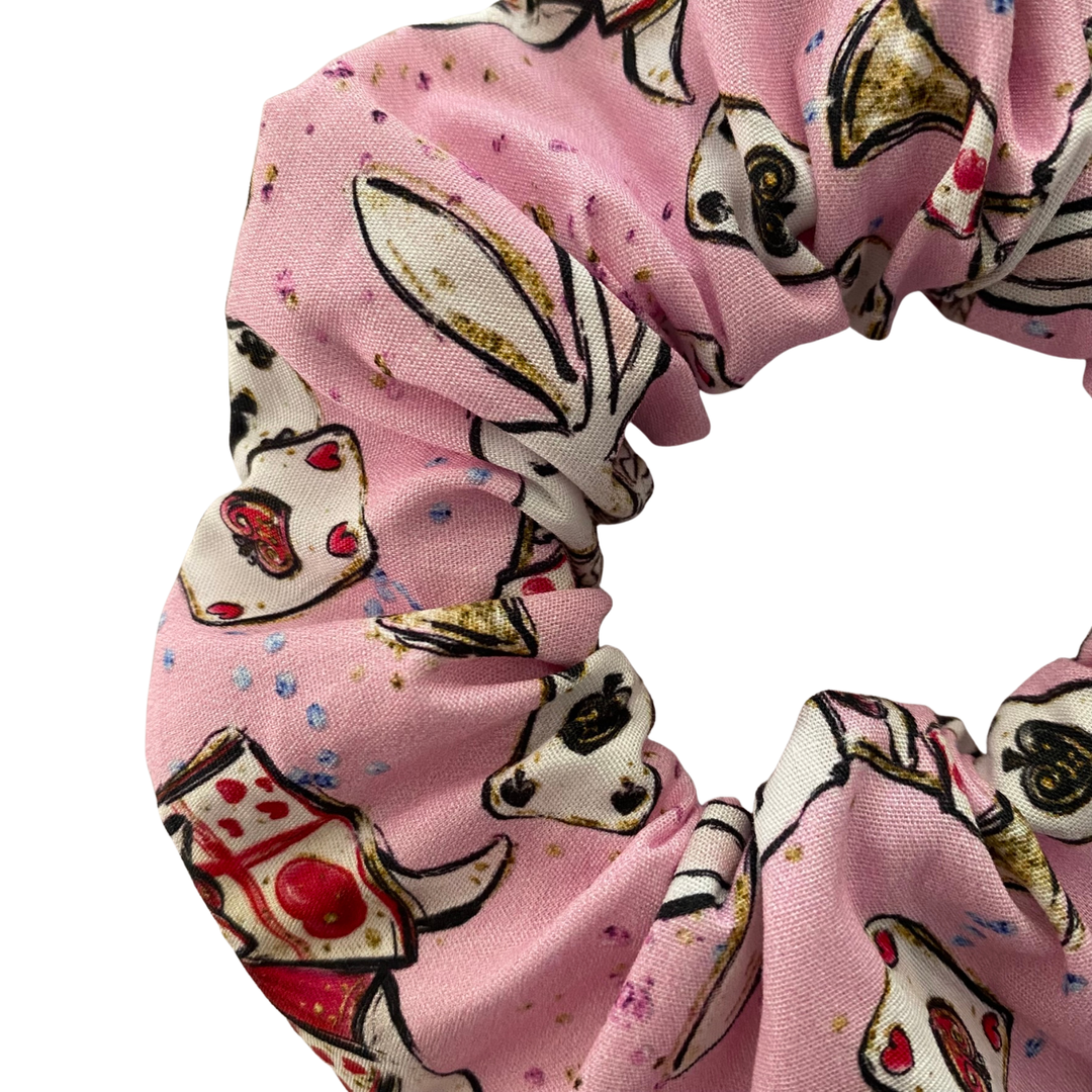 A close up view of a light pink fabric scrunchie with cartoon images of playing cards and white rabbit.