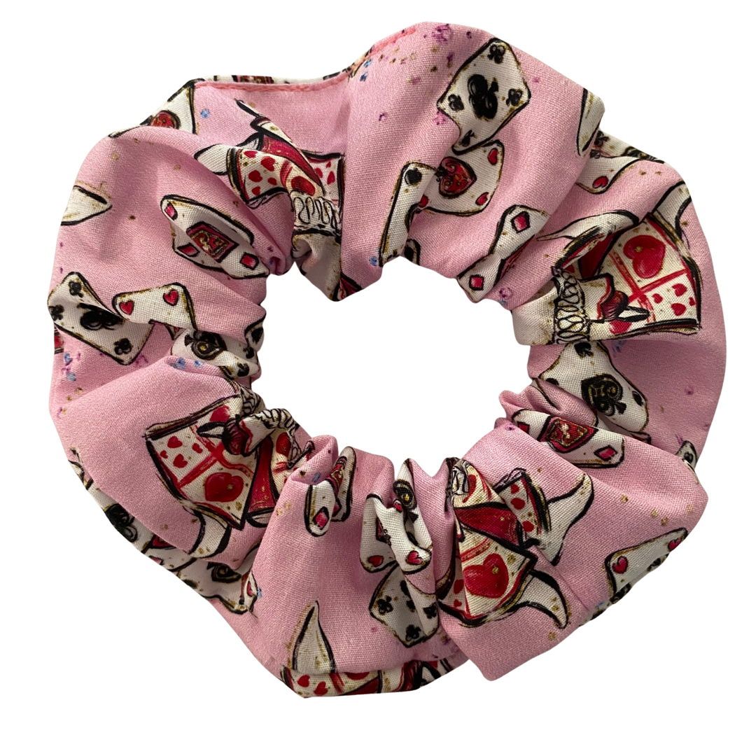 A light pink fabric scrunchie with cartoon images of playing cards and white rabbit.