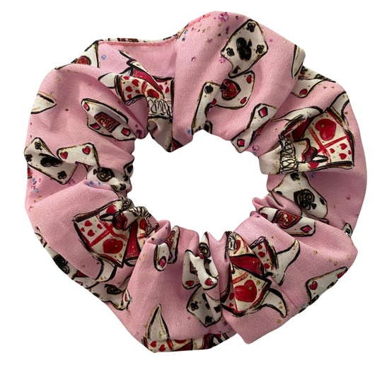 A light pink fabric scrunchie with cartoon images of playing cards and white rabbit.