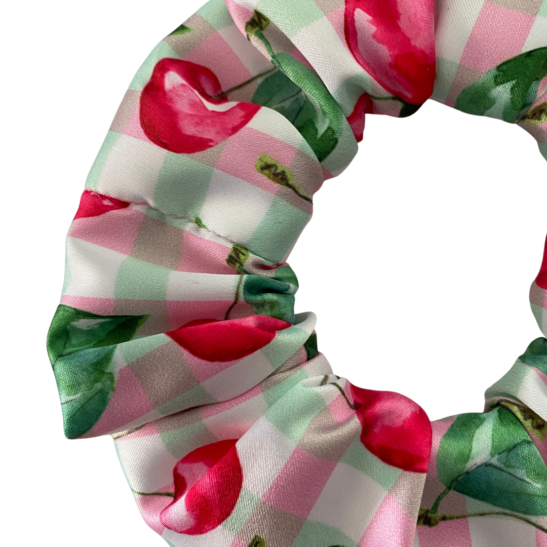 Satin scrunchie with cherry and checkered pattern on a white background.