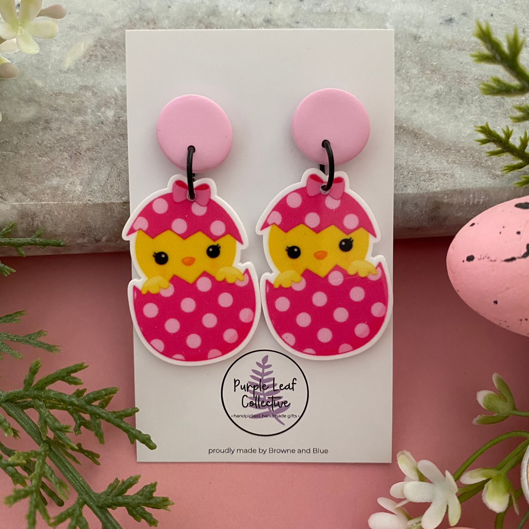 A pair of handmade dangle earrings featuring a sweet yellow chick peeking out of a colourful spotted Easter egg, designed for lightweight comfort.