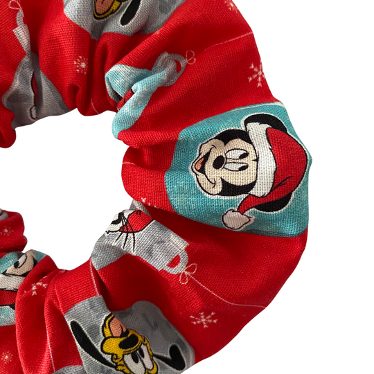 Close up view of red scrunchie with Mickey, Minnie, Donald, Daisy, Goofy character pattern on a white background.