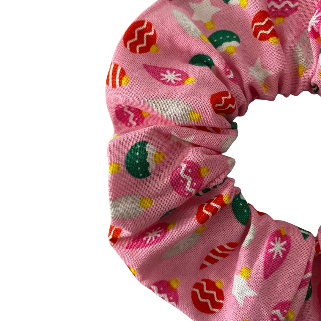 Close up view of a pink scrunchie with colourful baubles patterns on a pink fabric.