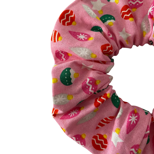 Close up view of a pink scrunchie with colourful baubles patterns on a pink fabric.