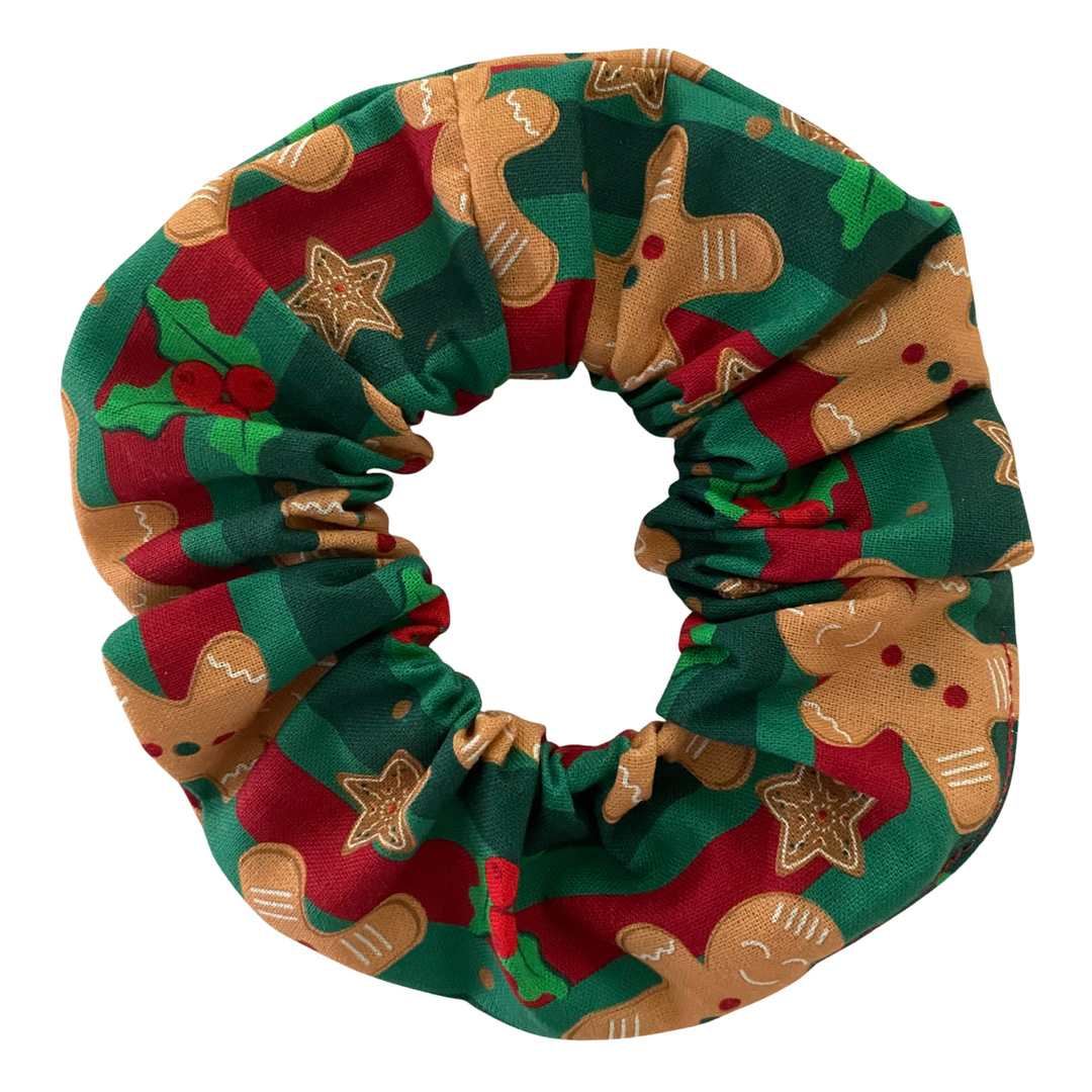 A medium-sized Christmas scrunchie featuring a pattern of gingerbread men and green holly leaves on a festive red and green striped cotton fabric.