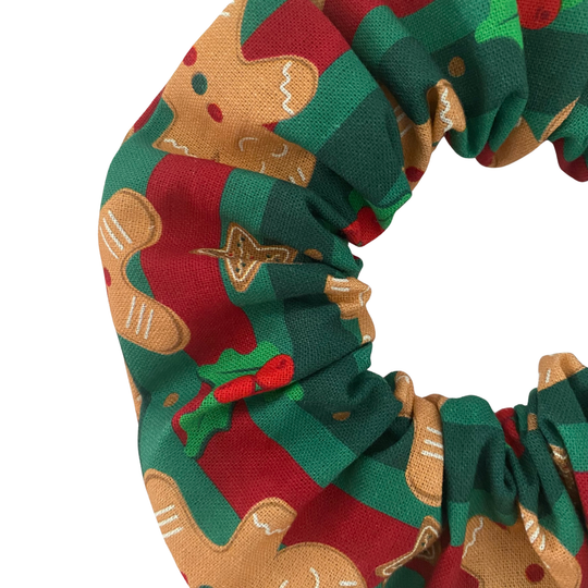 A Christmas scrunchie featuring a pattern of gingerbread men and green holly leaves on a festive red and green striped cotton fabric.