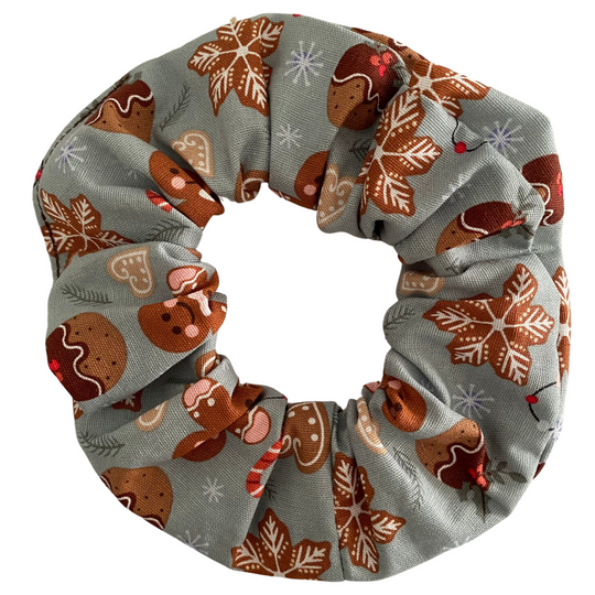 A scrunchie featuring images of gingerbread man and Christmas puddings on a light sliver fabric.
