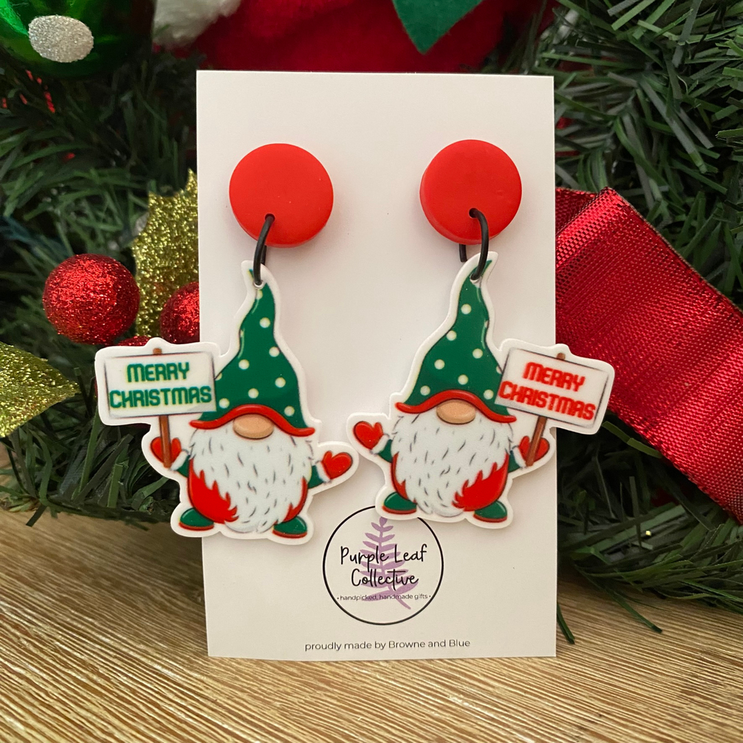 Pair of Christmas-themed gnome earrings on a card with 'Purple Leaf Collection' branding, surrounded by festive decorations.