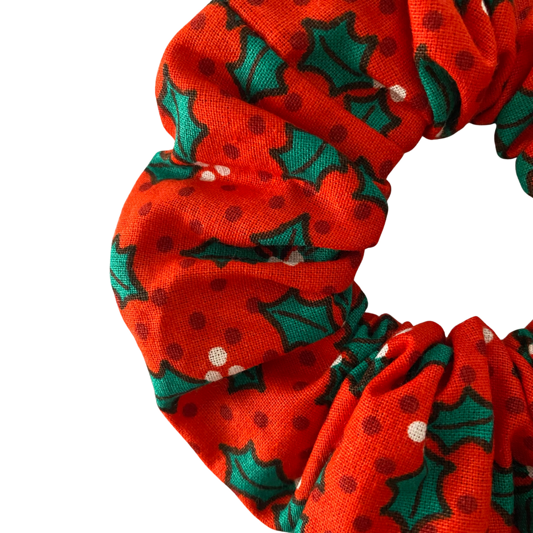 Green holly leaf scrunchie on a red fabric.