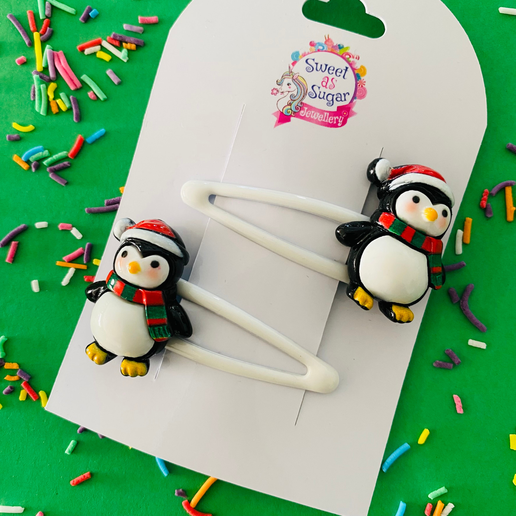 A pair of penguin charms wearing festive scarves and hats set on white hair clips.