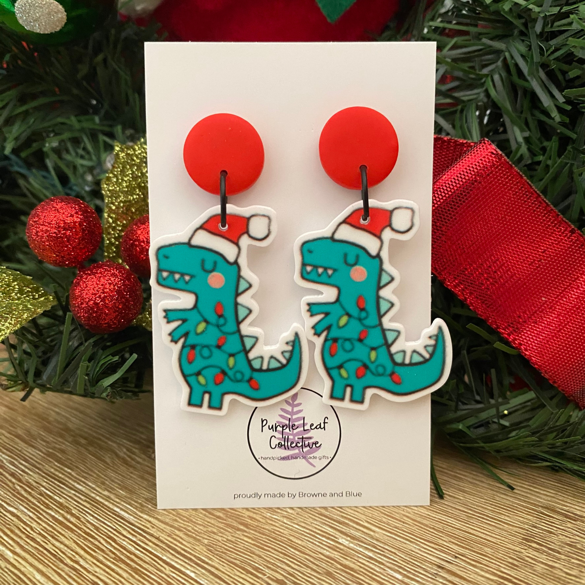 Dinosaur-shaped earrings on a card with Christmas decorations in the background.