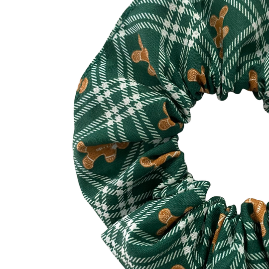 Close up view of a green plaid scrunchie with gingerbread men pattern on a white background.