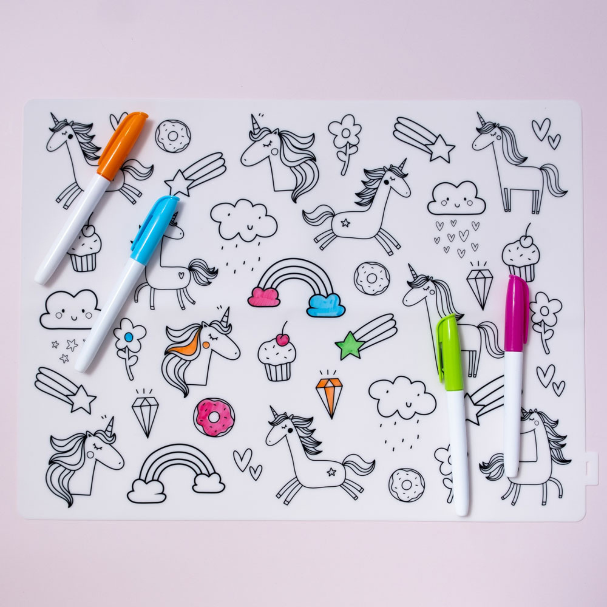 A picture of the Unicorn-themed Colour-In Silicone placemat showcasing whimsical images of Unicorns, Rainbows, Cupcakes and 4 nontoxic markers.