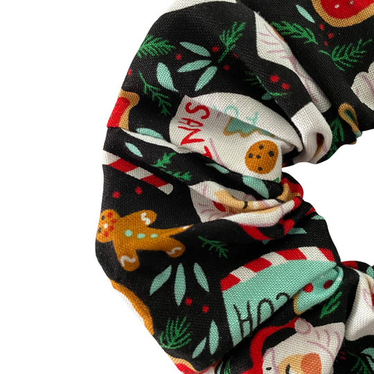 Close up view of cookies for Santa Christmas Scrunchie with cookies, candy canes and holly print on a black fabric. 