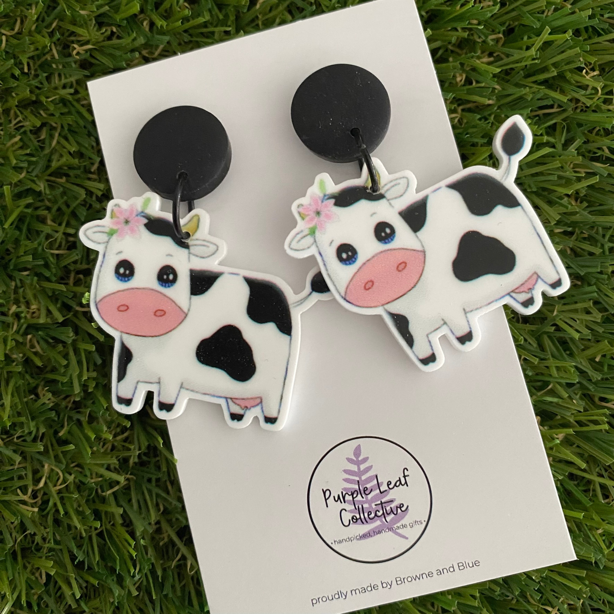 A pair of dangle earrings featuring two cute white-and-black spotted cows set on sleek black clay tops.