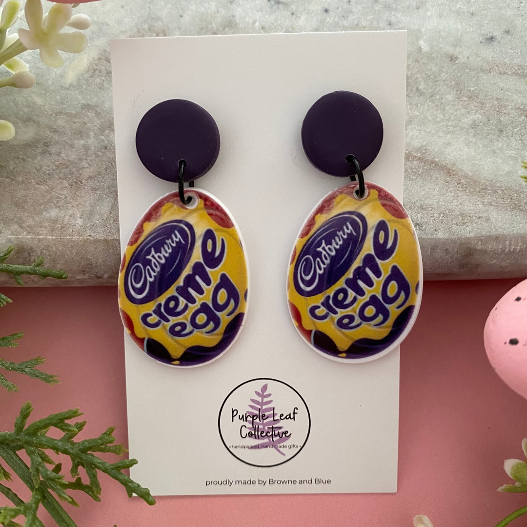 A pair of handmade dangle earrings inspired by a classic chocolate creme egg wrapper, featuring a vibrant purple, red, and yellow design.