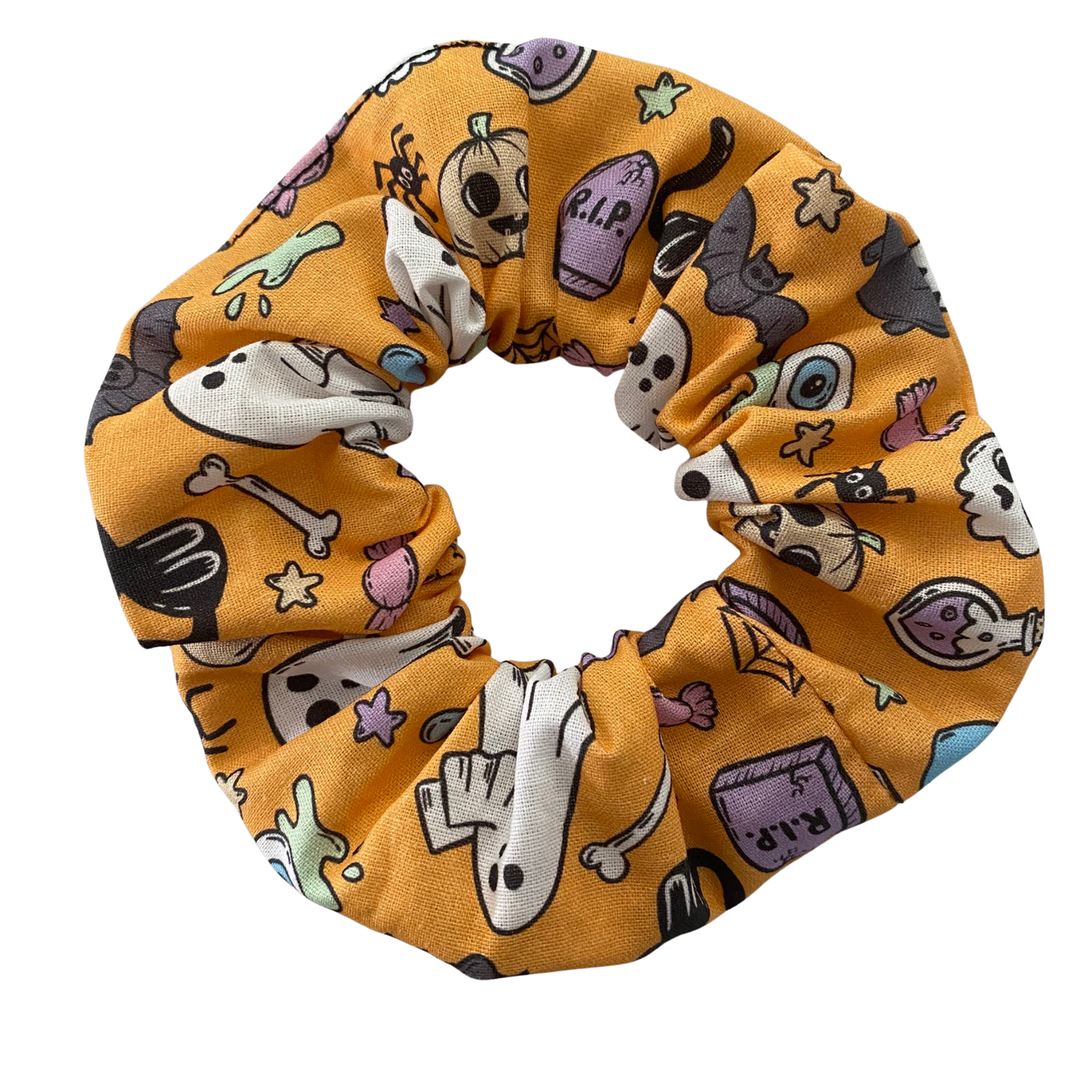 Halloween scrunchie featuring adorable collage of ghosts, pumpkins, coffins, cauldrons, bats and black cats on a light orange fabric.