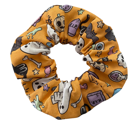 Halloween scrunchie featuring adorable collage of ghosts, pumpkins, coffins, cauldrons, bats and black cats on a light orange fabric.