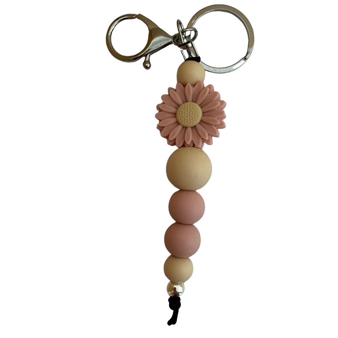 A keyring with a dusky rose daisy silicone bead and other assorted beads.