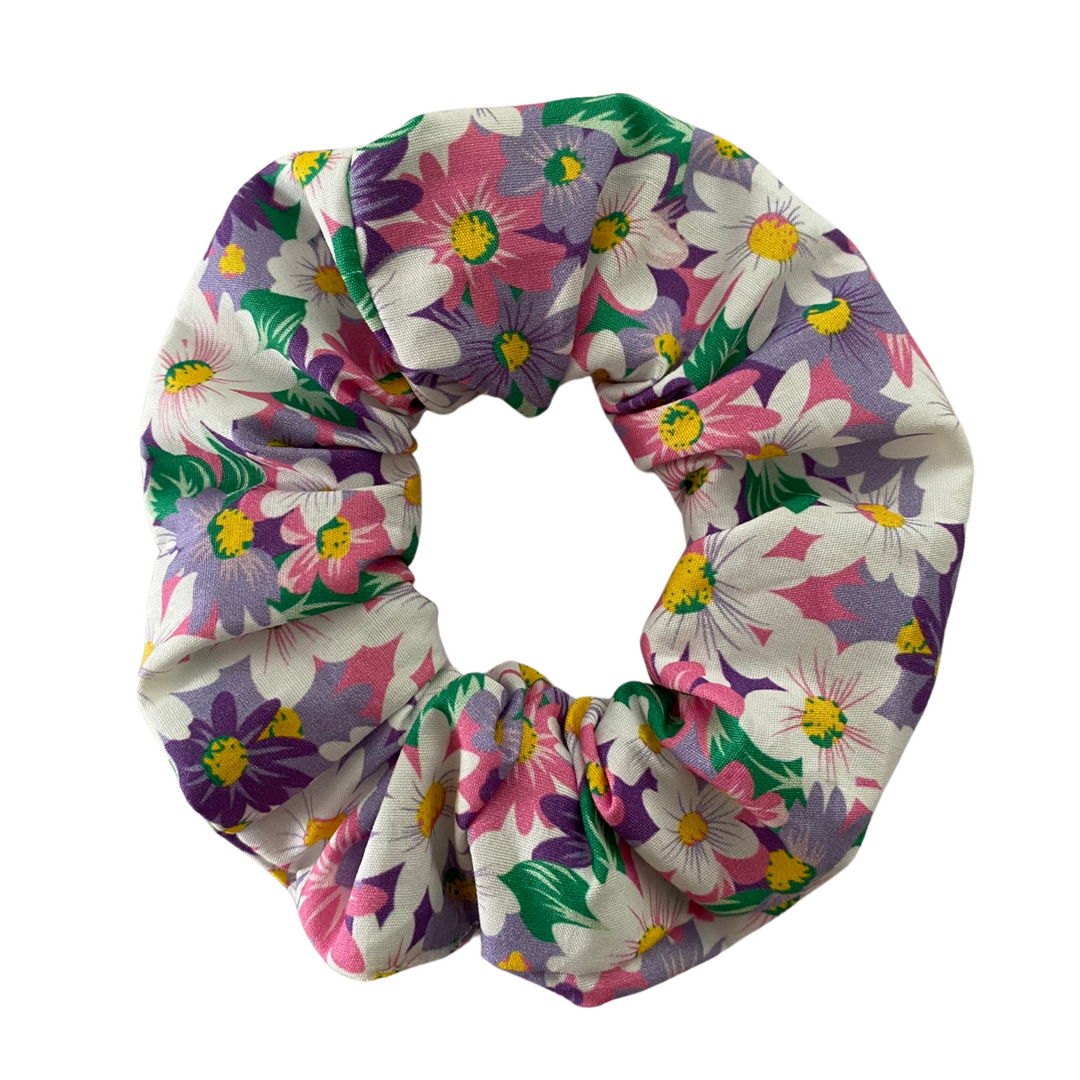 Daisy Fields Pinks Scrunchie is handmade from soft poplin fabric and features a mix of pink, purple, white, and lavender daisies. 