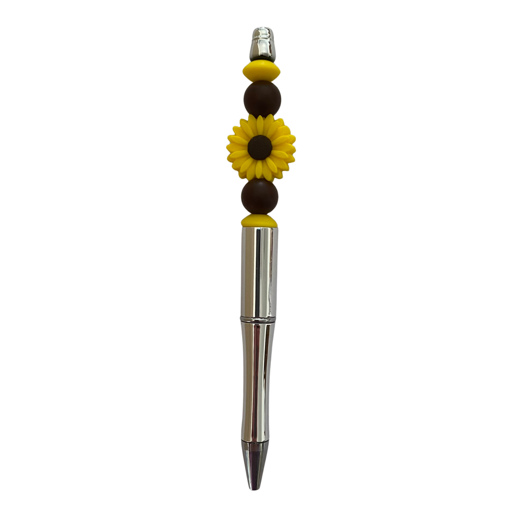 Pen with decorative daisy beads and a sunflower charm on a white background.