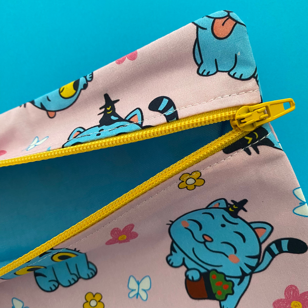 Lining view of pink pouch with cartoon cat design and yellow zipper on a blue background.