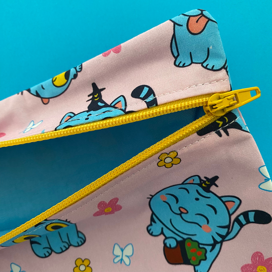 Lining view of pink pouch with cartoon cat design and yellow zipper on a blue background.