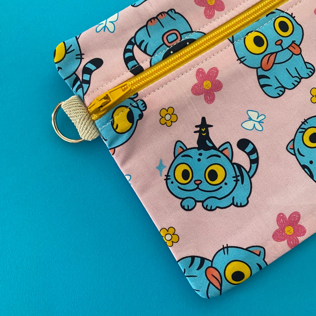 Side view of pouch with blue cat pattern on pink background against a blue background.
