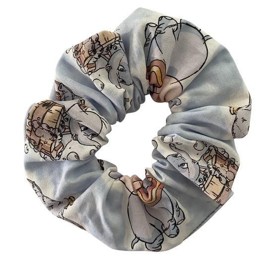 A scrunchie featuring playful images of Dumbo on a silver blue fabric on a white background.