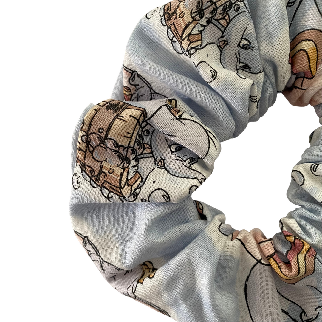 Close up view of a scrunchie featuring playful images of Dumbo on a silver blue fabric on a white background.