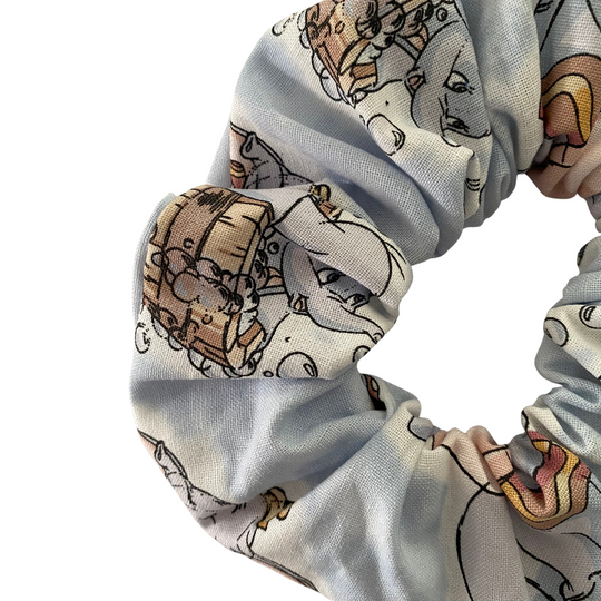 Close up view of a scrunchie featuring playful images of Dumbo on a silver blue fabric on a white background.