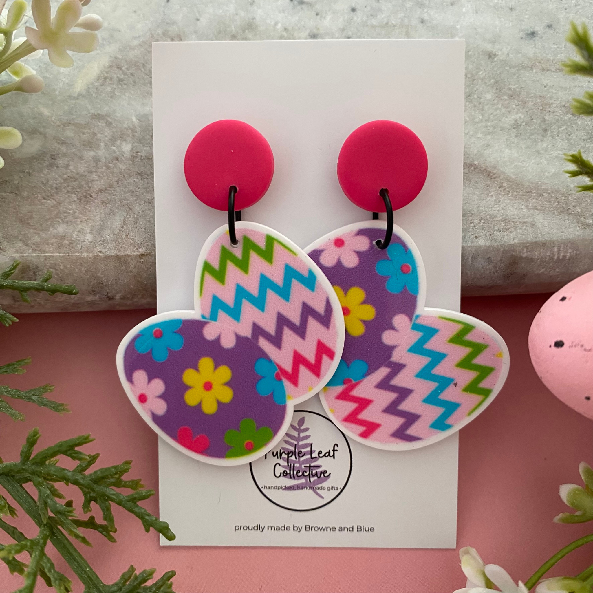 Pair of handmade Easter Egg dangle earrings featuring colourful flower and zig-zag patterns on a white background.