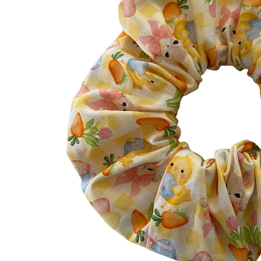 Scrunchie with Easter-themed design featuring bunnies, carrots and eggs on a yellow gingham pattern fabric.