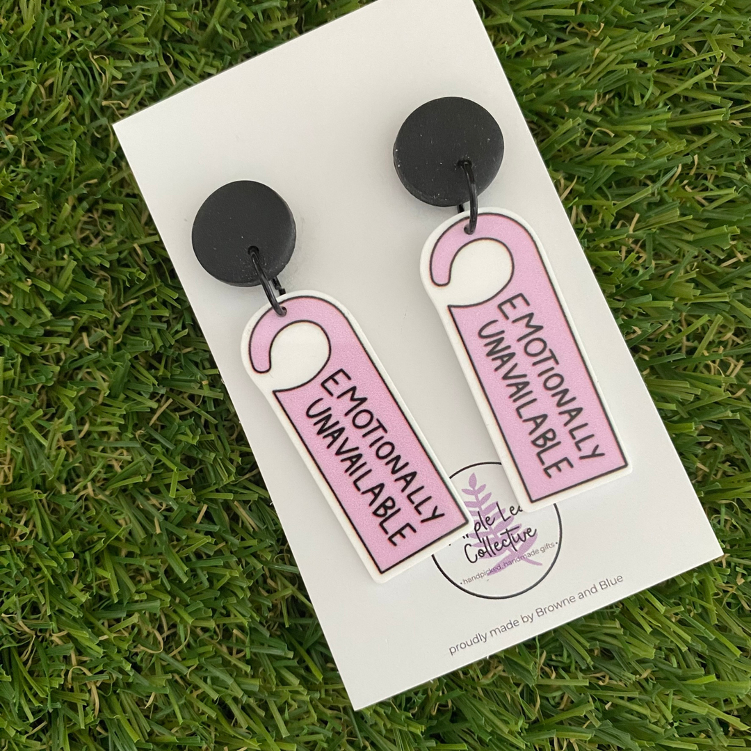 Pair of earrings with 'Emotionally Unavailable' tag design set on black clay stud tops.