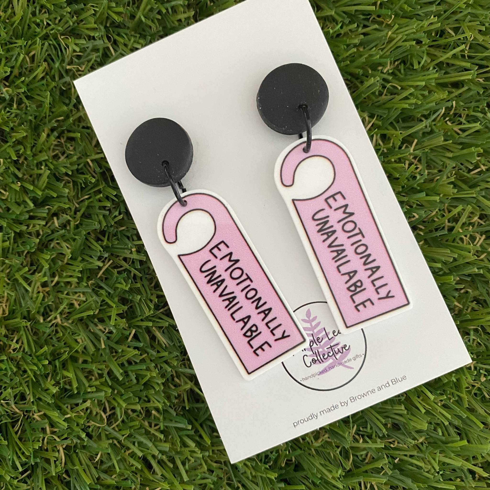 Pair of earrings with 'Emotionally Unavailable' tag design set on black clay stud tops.