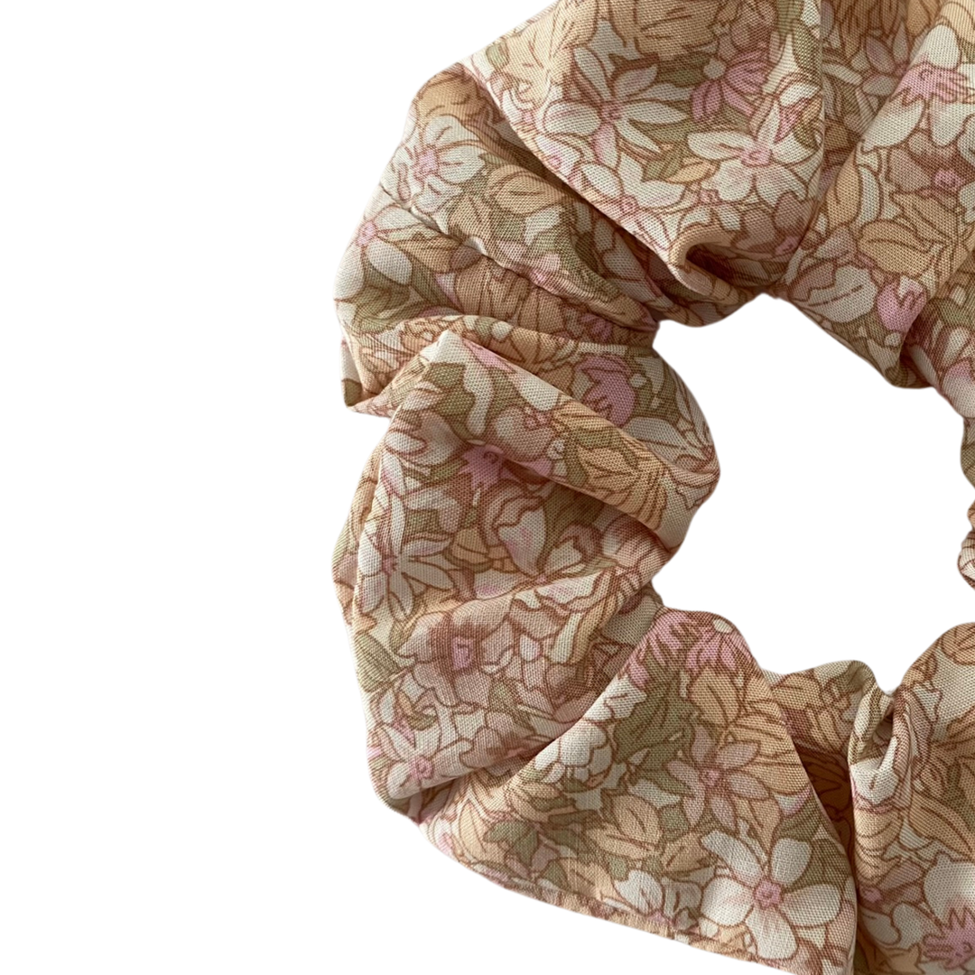 Close up view of a light pink floral scrunchie made from 100% viscose fabric with a dainty white and baby pink flower print.