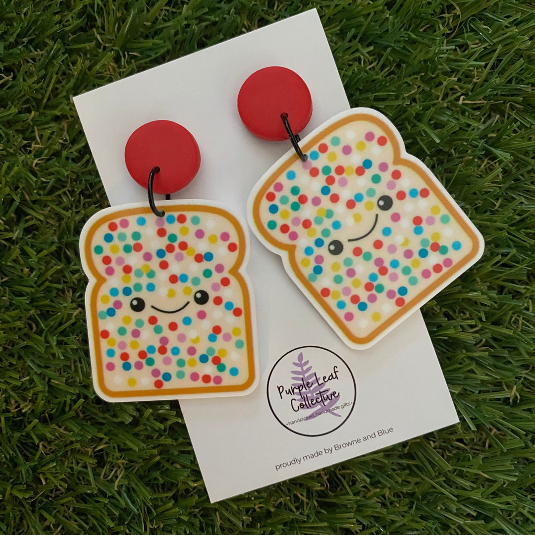 Featuring two slices of fairy bread complete with smiling faces and rainbow sprinkles, all set on red clay stud tops. 