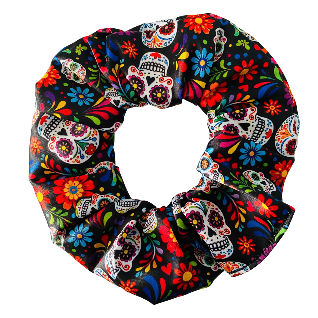 A satin hair scrunchie featuring a vibrant Day of the Dead sugar skull and floral pattern on black fabric.