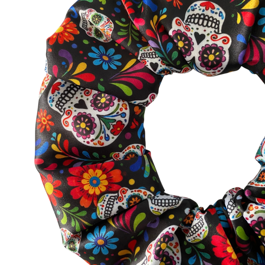 Close up view of a satin hair scrunchie featuring a vibrant Day of the Dead sugar skull and floral pattern on black fabric.