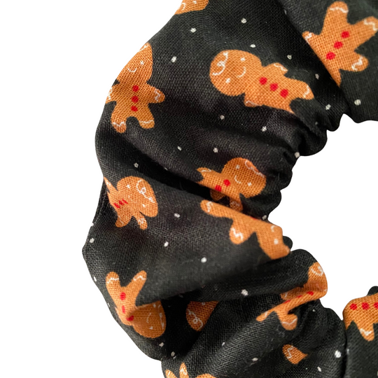 Close up view of a black scrunchie with gingerbread man pattern on a white background.