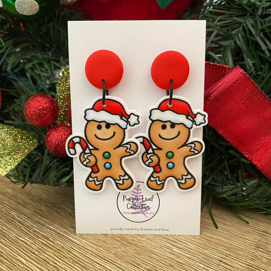 Gingerbread man earrings with Santa hats on a card with Christmas decorations in the background.