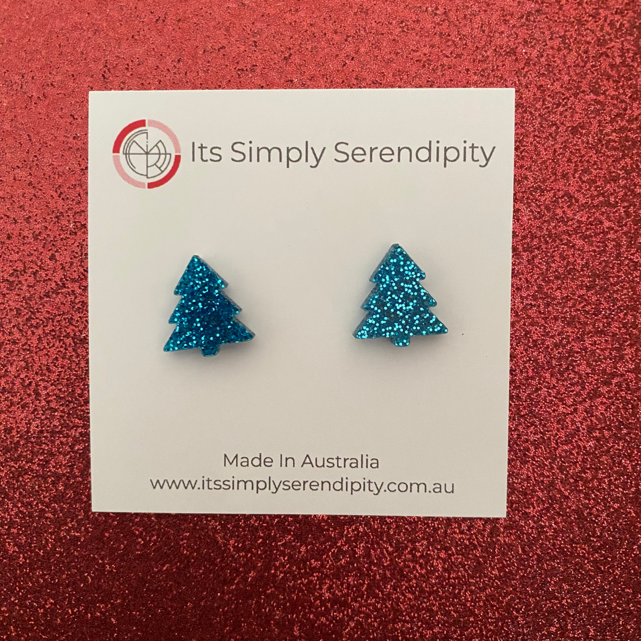 Blue glittery tree-shaped earrings on a 'Its Simply Serendipity' card with a red background.