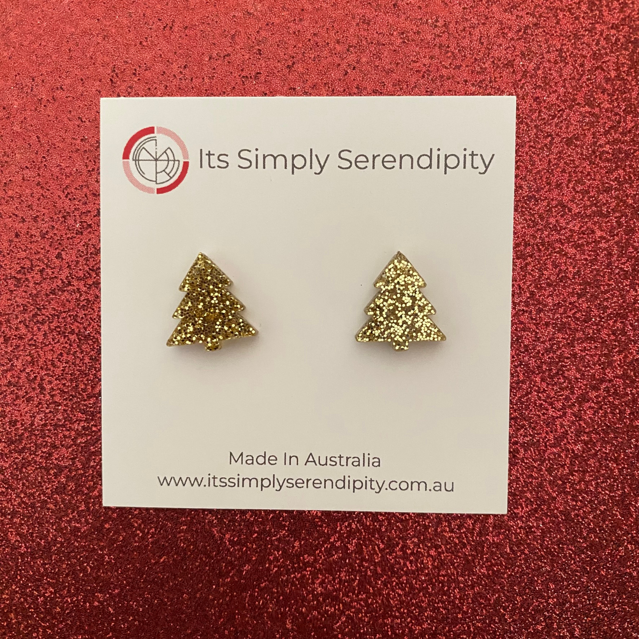 Gold tree-shaped earrings on a 'Its Simply Serendipity' card against a red background.