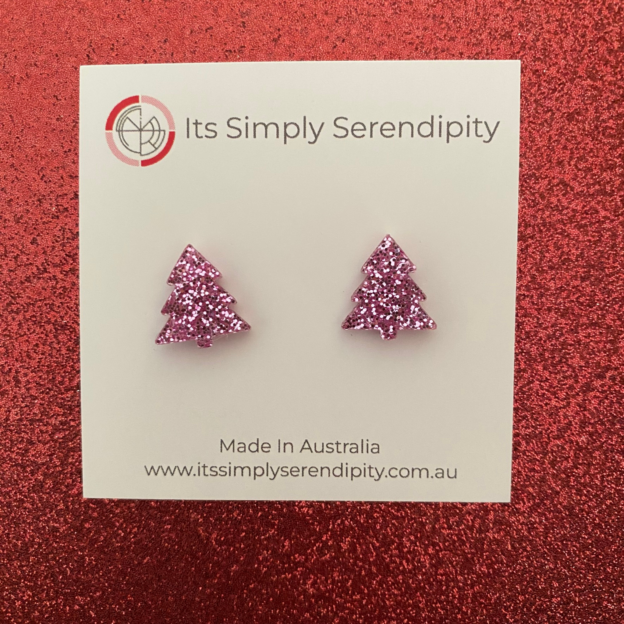 Pink glittery tree-shaped earrings on a 'Its Simply Serendipity' card against a red glittery background.