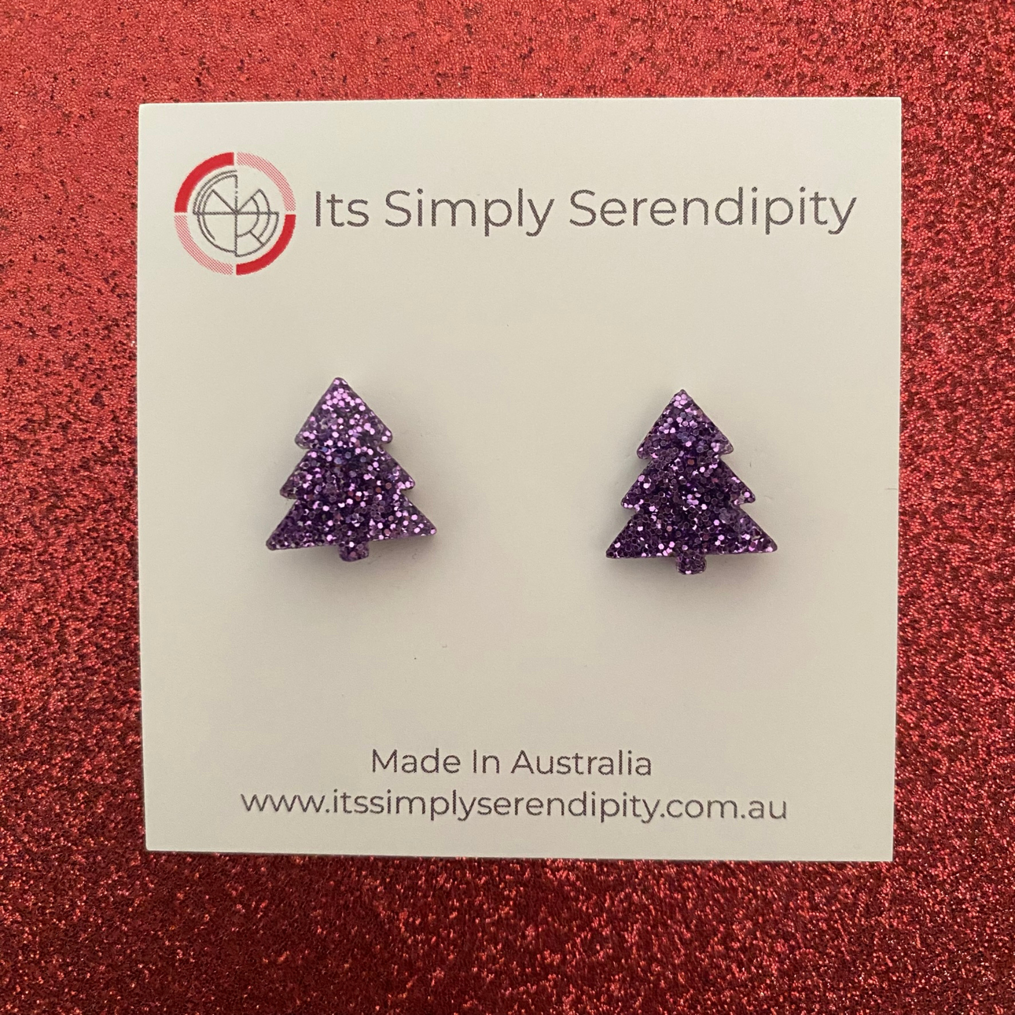 Purple glittery tree-shaped earrings on a 'Its Simply Serendipity' card with a red glittery background.