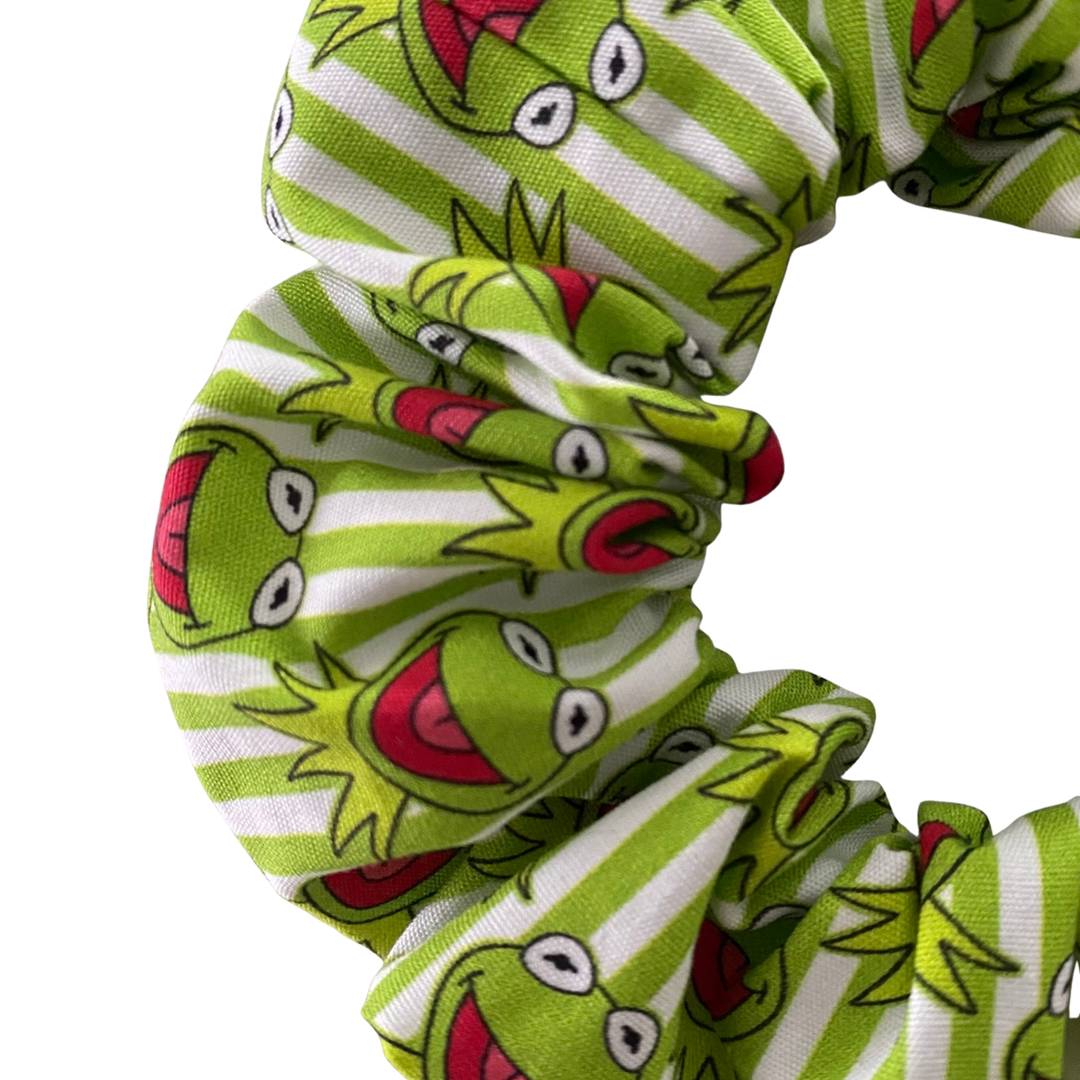Close up view of a green and white striped scrunchie with frog pattern on a white background.